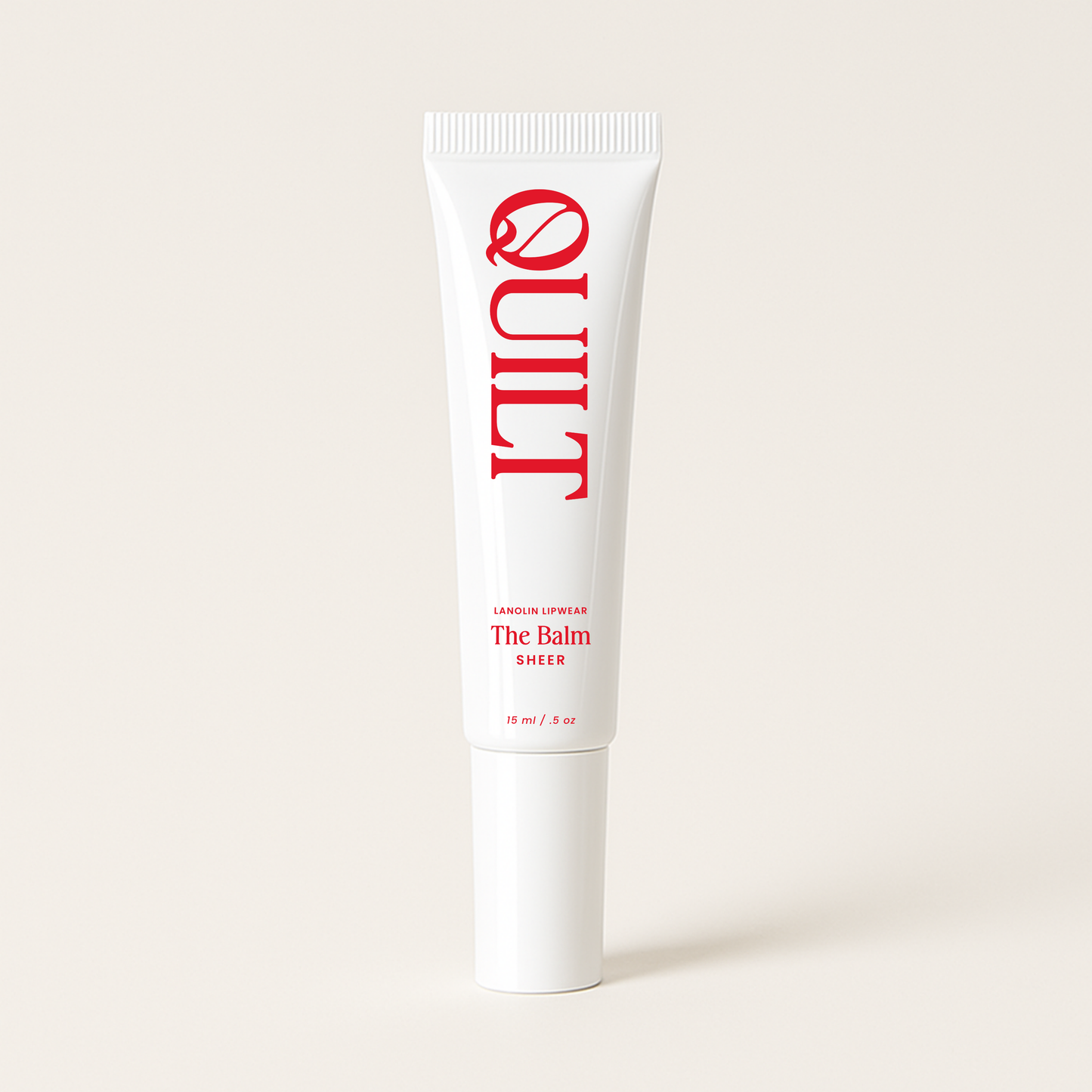 White tube of QUILT's lip balm - The Balm, with red text on a light beige background