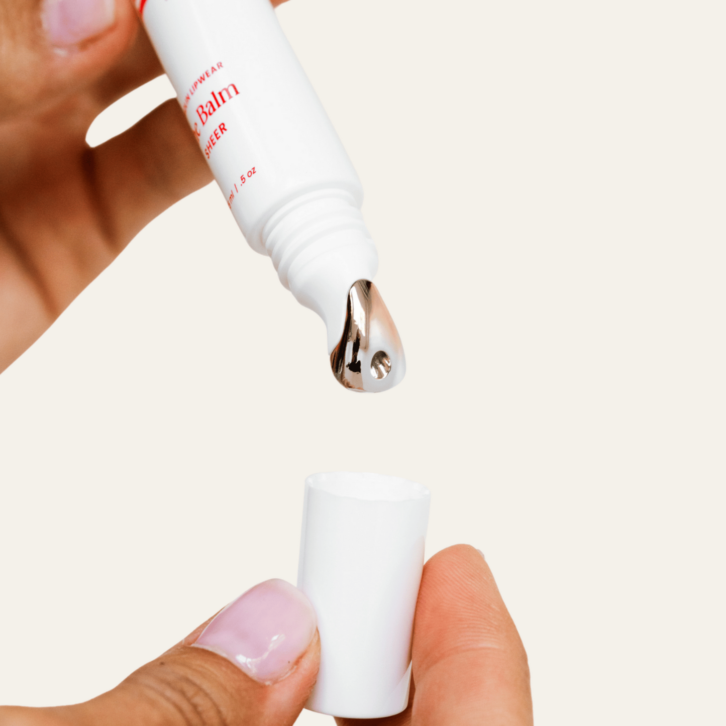 Hand holding a white lip gloss tube bottle with a metal cap, containing a cosmetic product.