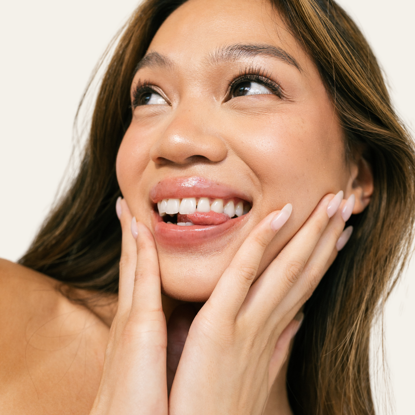 Woman with smooth skin and hydrated and nourished lips touching her face against a neutral background